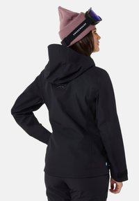 Sort udendørsjakke med en tætsiddende design, hætte og lynlåslommer. Bæres med en pink hue og skibriller. Diskrete logodetaljer er til stede.