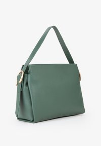 Borsa a mano in pelle verde con una forma strutturata, base piatta, manico corto e dettagli in hardware color oro. Texture liscia con una grana sottile.