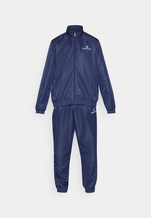 Marineblå joggedress laget av glatt, lett materiale; har en jakke med glidelås og bukser med elastisk midje, begge med logo-detaljer.