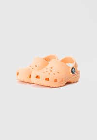 Oranžas koka kurpes no viegla materiāla, ar ventilācijas caurumiem, noapaļotu purngalu un aizmugurējo siksnu drošai pielāgošanai.