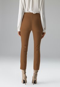 Braune, eng anliegende Hose mit hoher Taille und glatter Textur, kombiniert mit hellfarbenen, kniehohen Stiefeln mit Absatz. Weißes Langarmshirt sichtbar.