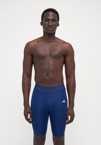 Sötétkék sportnadrágok, testhezálló fazonnal, rugalmas anyagból készült, magas derekú, oldalán egy kis fehér logóval.