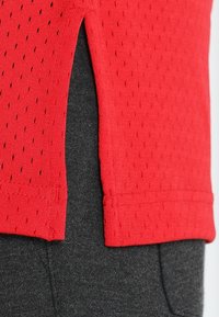 Roter strukturierter Stoff mit einem seitlichen Schlitz, der über einem dunkelgrauen glatten Stoff liegt und einen Kontrast in Material und Farbe zeigt.