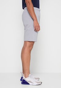 Pantaloncini sportivi grigi con vita elastica e tasche laterali, abbinati a scarpe da ginnastica bianche e grigie con accenti blu.