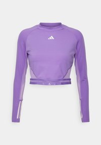 Fialový crop top s dlouhým rukávem vyrobený z hladké látky, s kulatým výstřihem a průhlednými síťovanými panely na rukávech. Ozdoben bílým logem.