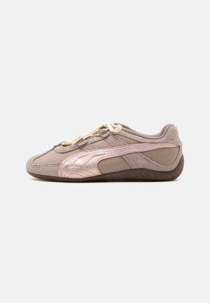 Baskets taupe profil bas avec textures en daim et cuir, lacets crème, et une bande métallique or rose le long du côté sur une semelle sombre.
