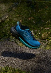Blau und schwarze Sportschuhe mit einer strukturierten Oberseite, gepolsteter Sohle und einem markanten Logo. Lebendige türkisfarbene Akzente an der Zwischensohle.