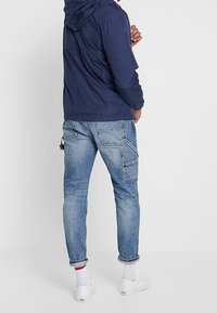 Marinblå huvjacka med avslappnad passform, kombinerad med ljusblå denimjeans med fickdetaljer och uppvikt fåll, som bärs med vita skor.