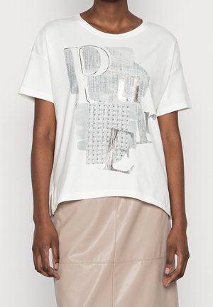 Person iført hvid kortærmet T-shirt med grå abstrakt tekst og mønster, kombineret med beige højtaljet nederdel.