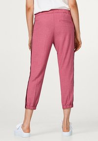 Roze cropped broek met een elastische tailleband, zijzakken en zwarte zijstrepen. De stof lijkt gestructureerd en lichtgewicht.