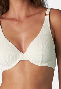 Reggiseno color crema con motivo testurizzato, supporto con ferretto e spalline regolabili con hardware in metallo.