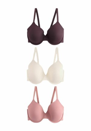 Femme aux longs cheveux foncés porte un soutien-gorge violet foncé et une lingerie en dentelle assortie, regardant droit avec une expression neutre sur un fond uni.