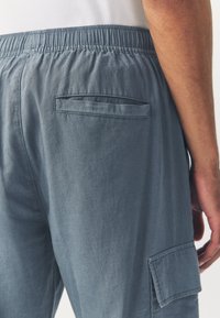 Grey cotton pants with an elastic waistband, featuring a rear pocket and a relaxed fit. Fabric has a smooth texture and slight sheen.