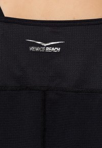 Camiseta deportiva sin mangas negra con tejido texturizado, diseño estructurado y un logo plateado que dice "VENICE BEACH" cerca del escote.