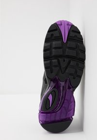 Svart atletisk skosula med mönstrad gummi, med en lila genomskinlig mellansula och synliga design detaljer för grepp.