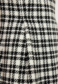 Schwarz-weißes Stoffmaterial mit Hahnentrittmuster, das eine ausgeprägte Textur und ein gewebtes Finish aufweist, mit einer Faltenstütze entlang der Naht.