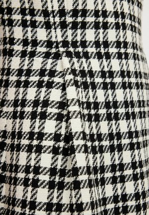 Kangast, millel on must-valge houndstooth mustril, eristuva tekstuuri ja kootud viimistlusega, sisaldab õmbluse juures voltide detaili.