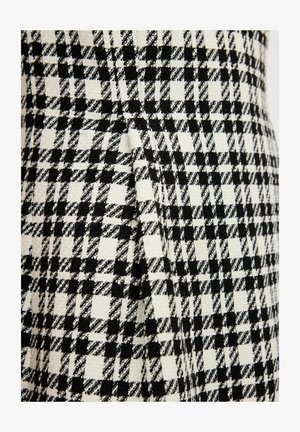 Černobílá tkanina s vzorem houndstooth, která má výraznou texturu a tkaný povrch, s přehybem podél švu.