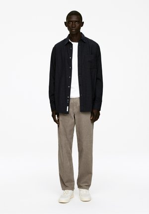 Dunkelblauses, kariertes Button-Up-Hemd, kombiniert mit hellgrauen, strukturierten Hosen und weißen Sneakers. Schlichtes, funktionales Design.