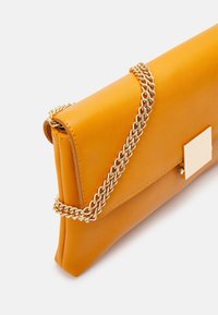 Clutch de cuero amarillo con una correa de cadena dorada, de forma rectangular, que presenta un acabado de hardware dorado cuadrado en el frente. Textura suave.