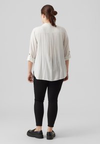 Lange mouw crèmekleurige blouse met opgerolde manchetten, achterkant met plooi-detaillering, gedragen over zwarte aangesloten broek en zwarte platform schoenen. Zachte stoftextuur.