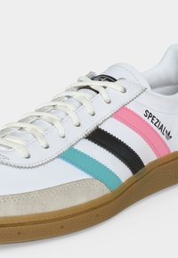 Λευκό παπούτσι Adidas Spezial με ροζ, μαύρες και μπλε ρίγες, λευκά κορδόνια, μπεζ μύτη και λαστιχένια σόλα.