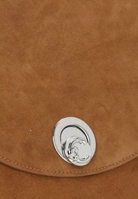 Borsa a tracolla in pelle scamosciata color beige con una texture liscia, dotata di un lucchetto circolare in argento lucido e cuciture dettagliate lungo i bordi.
