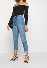 Svart off-shoulder ribbad topp i kombination med ljusblå högmidjade jeans. Svarta remmar med hög klack och en liten svart handväska.