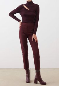 Burgundy ribbad turtleneck-top med en asymmetrisk skæring, kombineret med matchende tætsiddende bukser og ankelstøvler med blokhæle.