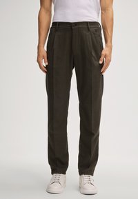 Ciemnozielone spodnie w kant wykonane z teksturowanej tkaniny, z paskami na pasek, zapięciem na guzik i bocznymi kieszeniami, w połączeniu z białymi sneakersami.