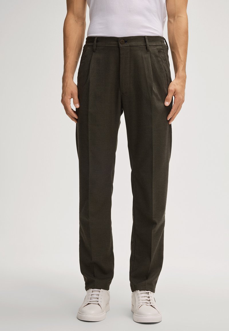 Ciemnozielone spodnie w kant wykonane z teksturowanej tkaniny, z paskami na pasek, zapięciem na guzik i bocznymi kieszeniami, w połączeniu z białymi sneakersami.