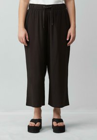 Zwarte, wijde broek gemaakt van zacht materiaal met een elastische tailleband en trekkoord. De zoom is net boven de enkel afgerond.