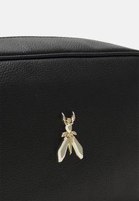 Schwarze, strukturierte Lederhandtasche mit einem goldenen Insektenlogo-Akzent auf der Vorderseite, das die filigranen Details im Design hervorhebt.