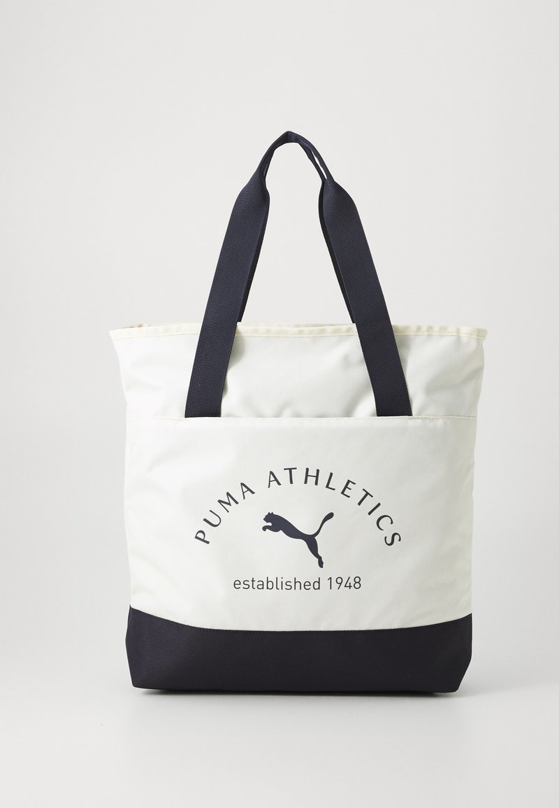 Puma Athletics draagtas, met een roomkleurige bovenkant, een marineblauwe basis en contrasterende handvatten. Bedrukt logo en oprichtingsjaar in donkere tekst.