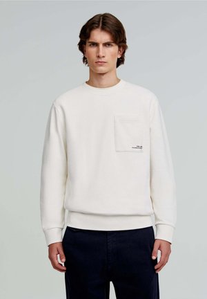 Sweatshirt crème en tissu doux, avec un col rond, des poignets côtelés, une poche poitrine et un détail de texte imprimé. Assorti avec un pantalon bleu marine.