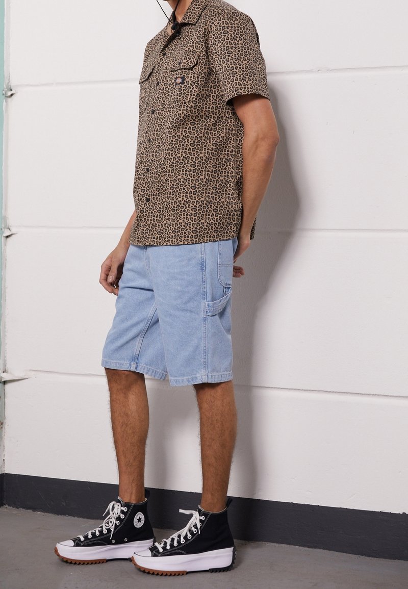 Košile s krátkým rukávem s leopardím potiskem v hnědých tónech, doplněná světle modrými cargo šortkami a černými vysokými teniskami, které mají bílé tkaničky a gumovou podrážku.