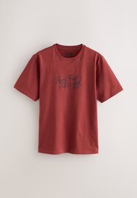 T-shirt rouge en coton à manches courtes, col rond, avec un motif graphique affichant "Roam Free" accompagné d'un dessin de scorpion. Dos uni.