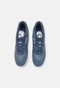 Sneaker blu in mesh e suede con colletto imbottito, presentano un logo bianco, lacci piatti e una suola in gomma di colore chiaro.