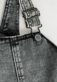 Los petos de mezclilla en blanco y negro presentan una tela texturizada, un broche metálico ajustable, costuras contrastantes y un patrón a cuadros distintivo.