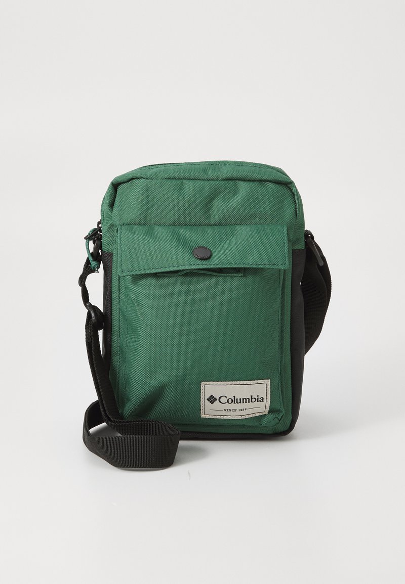 Borsa a spalla Columbia verde e nera di piccole dimensioni con tasca anteriore a patta e tracolla nera regolabile su sfondo bianco.