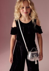 Abito di velluto nero con rouches a spalle scoperte, abbinato a una piccola borsa a tracolla metallica argento con chiusura a forma di cuore.
