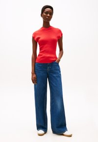Maglietta rossa a coste a maniche corte abbinata a jeans in denim blu a gamba larga e sneaker bianche. L'outfit presenta una silhouette aderente e uno stile casual.