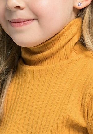 Suéter de cuello alto acanalado en color mostaza, textura suave, diseño ajustado. Pendiente pequeño en forma de flor en la oreja izquierda.