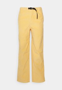 Żółte spodnie z korduroy w prostym kroju, z elastycznym pasem i czarnym sznurkiem do regulacji długości.