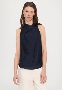Merijadikan ilman leher tanpa lengan dengan desain drap yang halus, tekstur mulus, dan leher tinggi. Terdapat kain lembut yang menggantung dengan elegan di sekitar bahu.