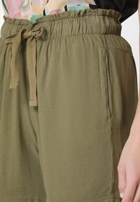 Olivgrön shorts med elastisk midja, dragsko och sidofickor. Tillverkade av mjukt, lätt material med en slät yta.