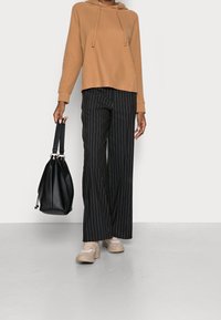 Brązowa bluza z kapturem, czarne szerokie spodnie w paski, beżowe sneakersy i czarna torba na sznurki. Skoncentrowano się na casualowym, luźnym fasonie.