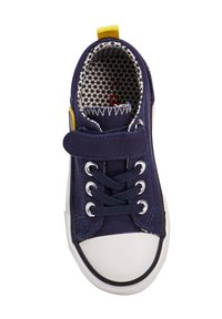 Baskets en toile navy avec un bout en caoutchouc blanc, lacets en tissu et une sangle Velcro. L'intérieur présente une doublure à motifs et une boucle de talon jaune.