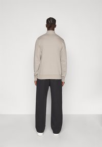 Ανοιχτό γκρι φούτερ με ψηλό γιακά, συνδυασμένο με φαρδιά σκουρόχρωμη γκρι παντελόνια. Απαλή υφή με ριμπ μανσέτες και τελείωμα.