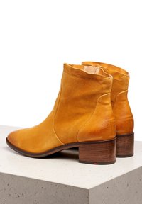 Žluté kožené kotníkové boty s hladkým povrchem, zaoblenou špičkou a nízkým dřevěným podpatkem. Navrženy s jemnými bočnými panely a minimálním prošíváním.